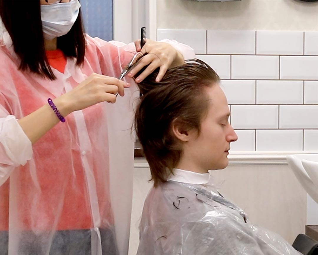 Парикмахер стрижет волосы парню